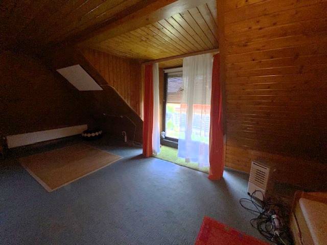 Ein Dachzimmer mit Holzverkleidung in einem Einfamilienhaus, Vorhänge über dem Fenster.