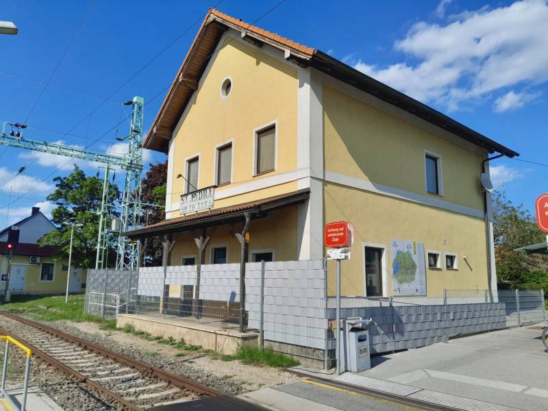 Das gelbe Bahnhofsgebäude in St. Andrä am Zicksee mit einem Hinweis auf die Züge.
