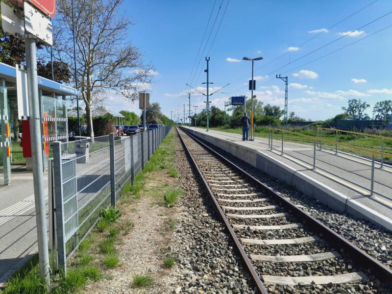 Bahnhof in St. Andrä am Zicksee mit Gleisen und einem Passagier auf dem Bahnsteig.