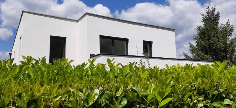 Villa in Hainburg an der Donau mit weißer Fassade, umgeben von Grün unter blauem Himmel.