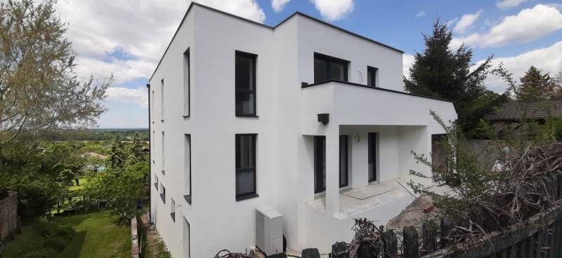 Eine Villa in Hainburg an der Donau mit weißer Fassade, umgeben von Grün und blauem Himmel.