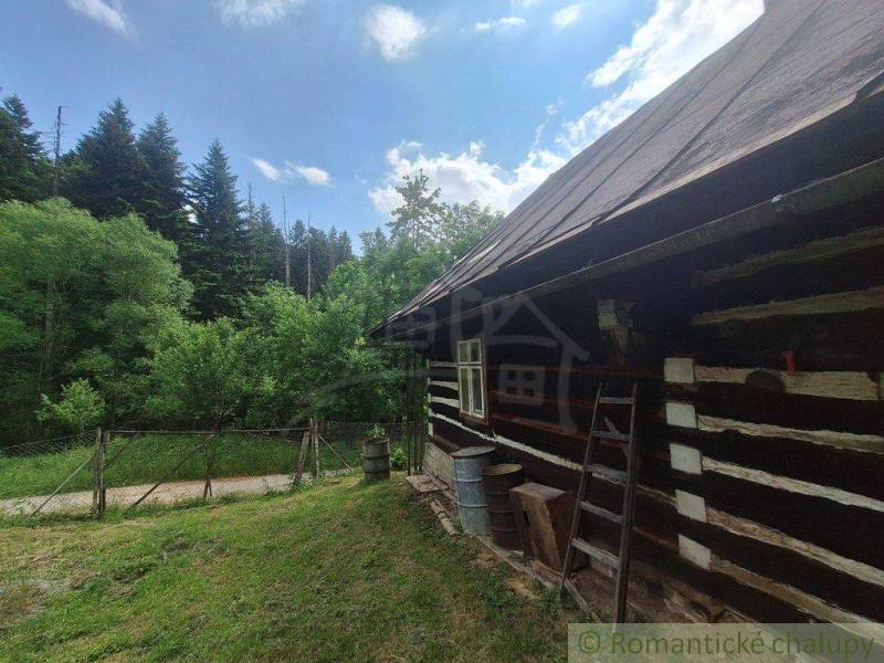 Eine Hütte in Zákopčí, umgeben von Wald, Holzwände, Zaun und blauer Himmel.