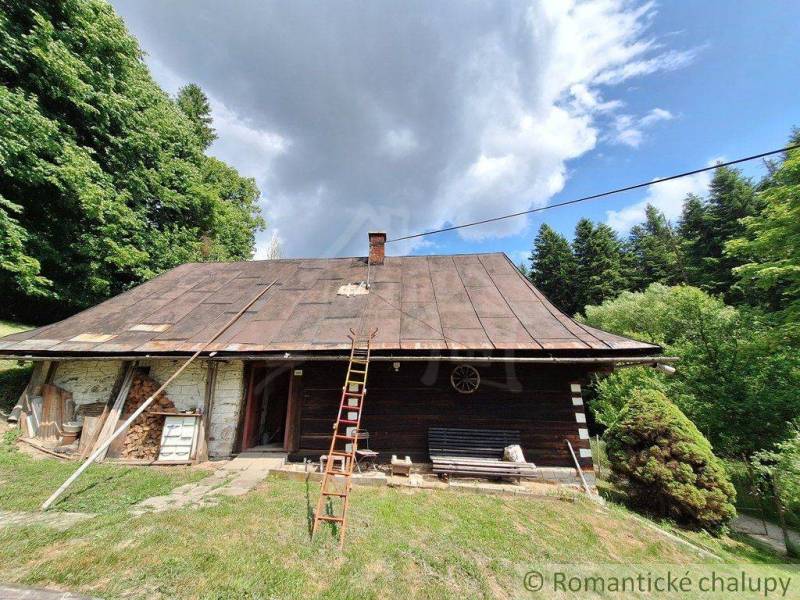 Rustikale Hütte in Zákopčie, umgeben von Wäldern und dramatischen Wolken am Himmel.