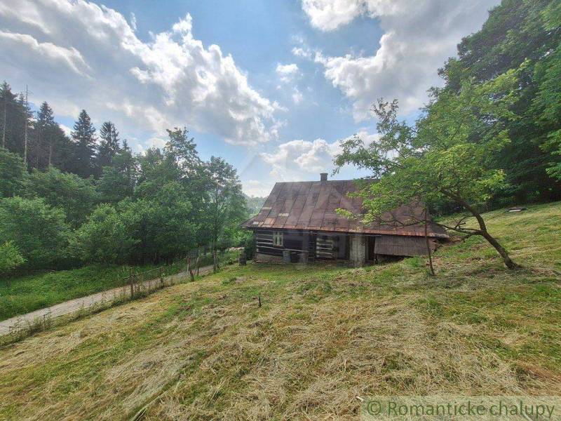 Eine Blockhütte in Zákopčí, umgeben von Wiesen und Wäldern, unter einem blauen Himmel mit Wolken.
