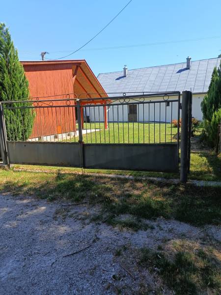 Ein Tor und eine Holzhütte in Tužina, umgeben von Rasen und Nadelbäumen.