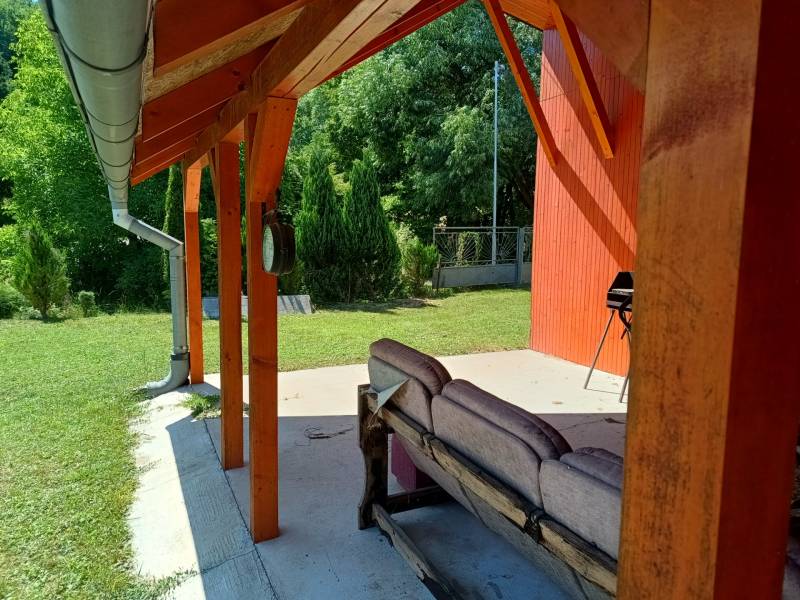 Eine Veranda bei der Hütte in Tužina mit Sitzgelegenheiten und einem Grill, umgeben von Grün.