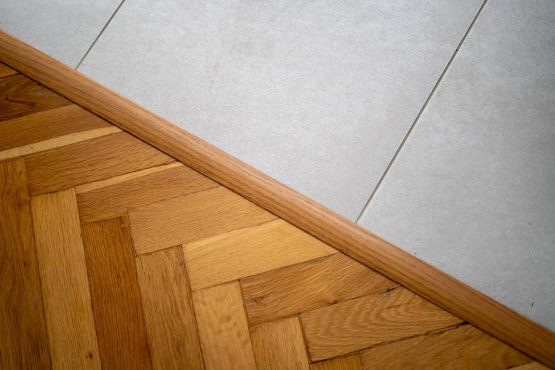 Übergang zwischen Holzboden und weißen Fliesen in einer 3-Zimmer-Wohnung.