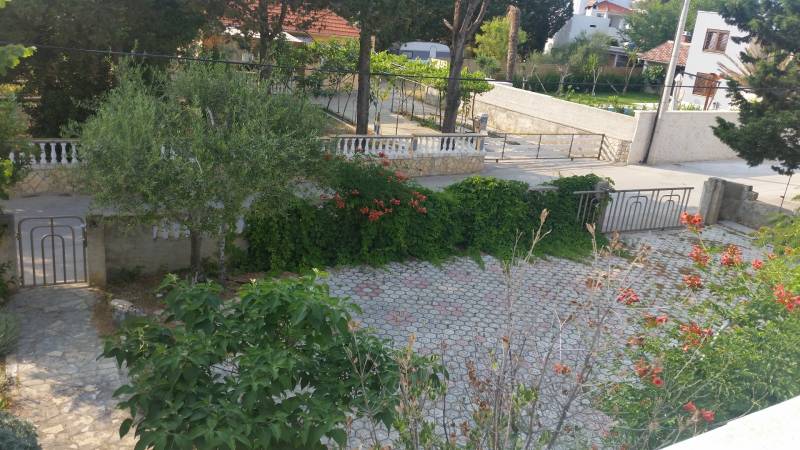 Der Garten des Einfamilienhauses in Vrsi mit Pflastersteinen, Grünflächen und Blumen.