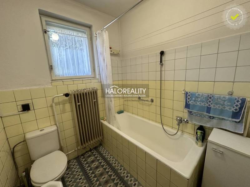 Ein Badezimmer in einem Einfamilienhaus mit Badewanne, Heizkörper und Fenster, dekoriert mit Fliesen.