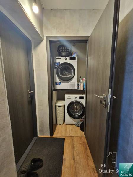 Ein schmaler Flur in einem Einfamilienhaus mit Waschmaschine und Trockner, Holzboden und dunklen Türen.