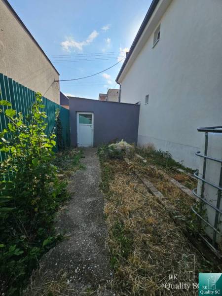 Das Einfamilienhaus in der Rybničná-Straße in Veľká Mača, ein schmaler Hof mit Grünflächen und einem Betonweg.
