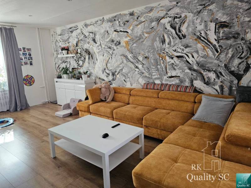 Wohnzimmer in einem Einfamilienhaus mit gelbem Sofa und abstrakter Wand mit bunten Pinselstrichen.