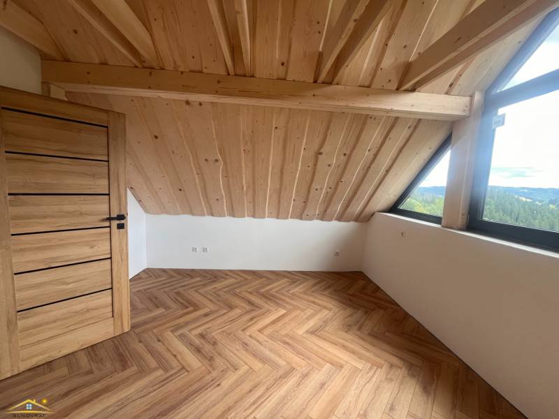 Dachzimmer in einer Hütte mit Holzdecke, großem Fenster und Parkettboden.