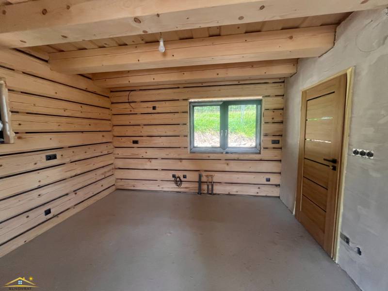 Innenraum einer Hütte mit Holzwänden, einem Fenster und einfacher Beleuchtung.
