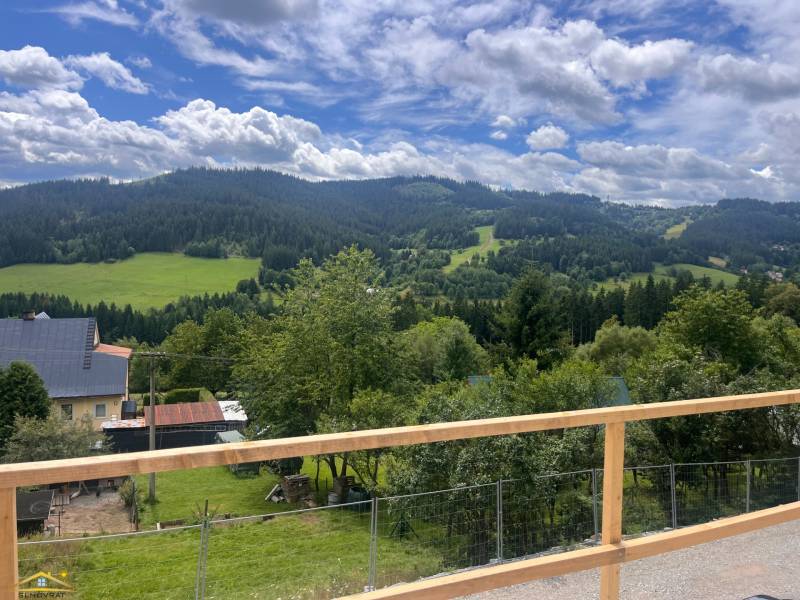 Der Ausblick von der Hütte in Korňa umfasst grüne Wiesen, Hügel und einen Himmel mit Wolken.