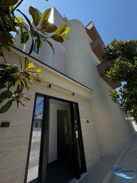 Die Fassade eines Ferienapartments in Ksamil, umgeben von Grün und klarem Himmel.