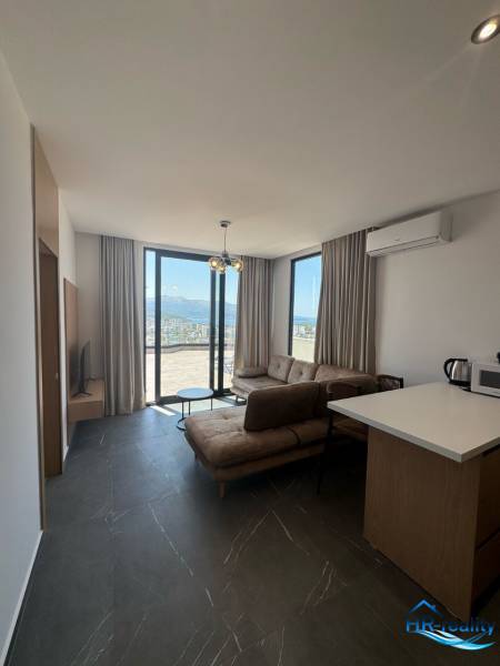 Wohnzimmer in einer Ferienwohnung mit großen Fenstern, Sofa und Küchenzeile.