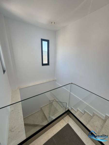 Treppe in einer Ferienwohnung mit großem Glasgeländer und schmalem Fenster.