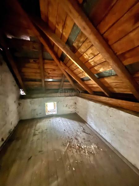 Dachbodenraum in einem Einfamilienhaus mit Holzbalkendecke und kleinem Fenster.