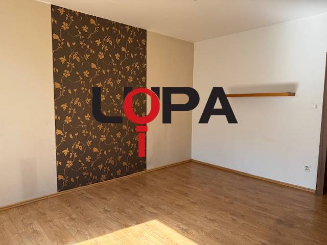 Ein leerer Raum mit Holzboden und gemusterten Tapeten in einer 3-Zimmer-Wohnung.
