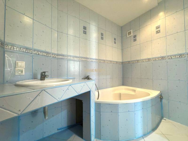 Ein Badezimmer mit hellblauen Fliesen und einer Eckbadewanne in einer Vierzimmerwohnung.
