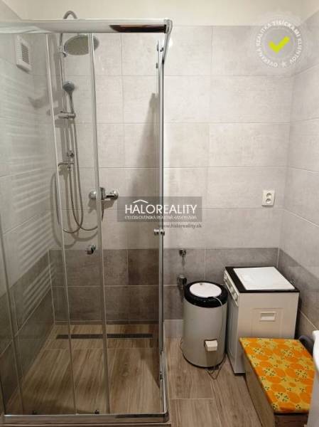 Duschkabine und Waschmaschine im Badezimmer für eine Zweizimmerwohnung mit braunen Fliesen.