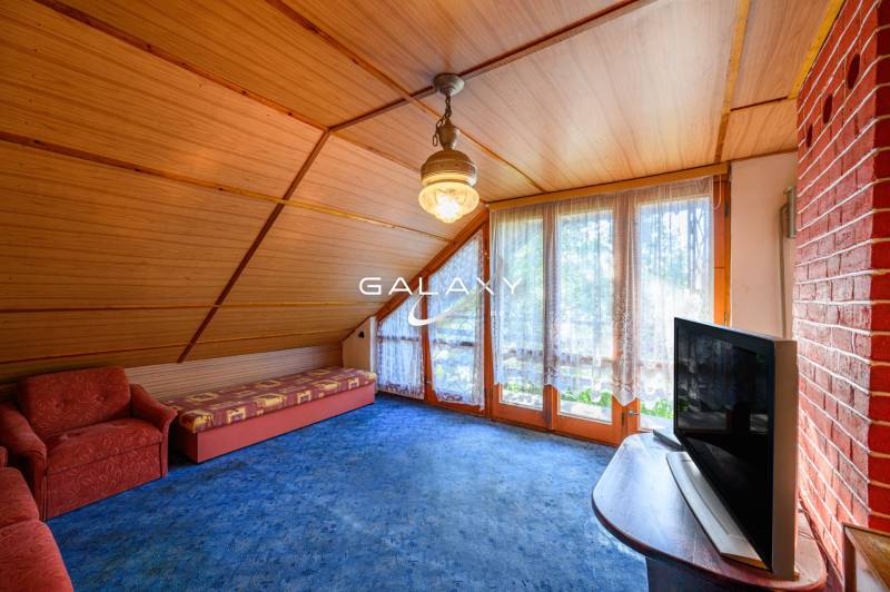 Ein gemütlicher Raum in einer Hütte mit einem Sessel, einem Sofa, einem Fernseher und großen Fenstern mit Aussicht.