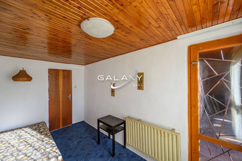 Holzdecke, Bett, Tisch, blauer Teppich, Lampe an der Wand in der Hütte.