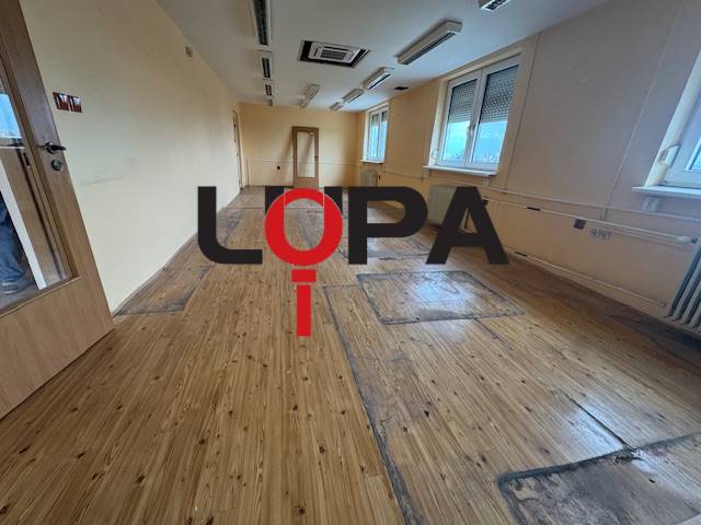 Zu vermietender Raum in einem Gebäude mit Holzboden, angeboten von einem Immobilienbüro.