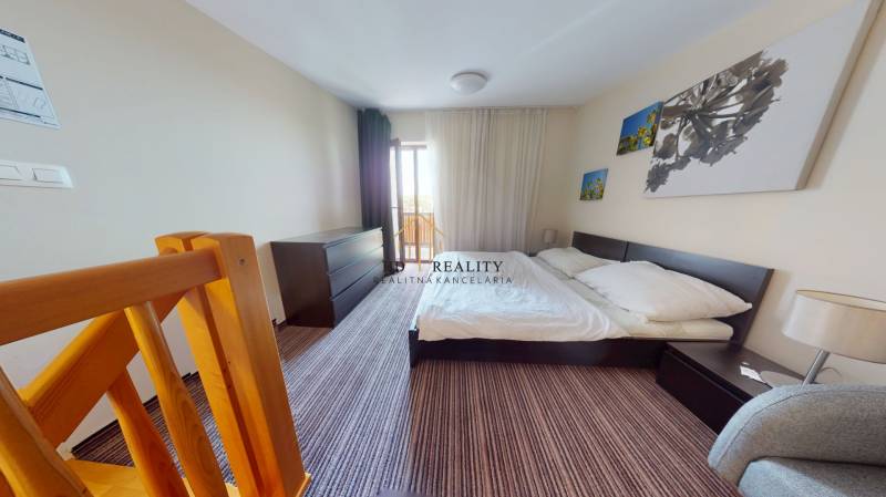 Schlafzimmer in einer Zweizimmerwohnung mit Treppe, großem Bett und Fotos an der Wand.