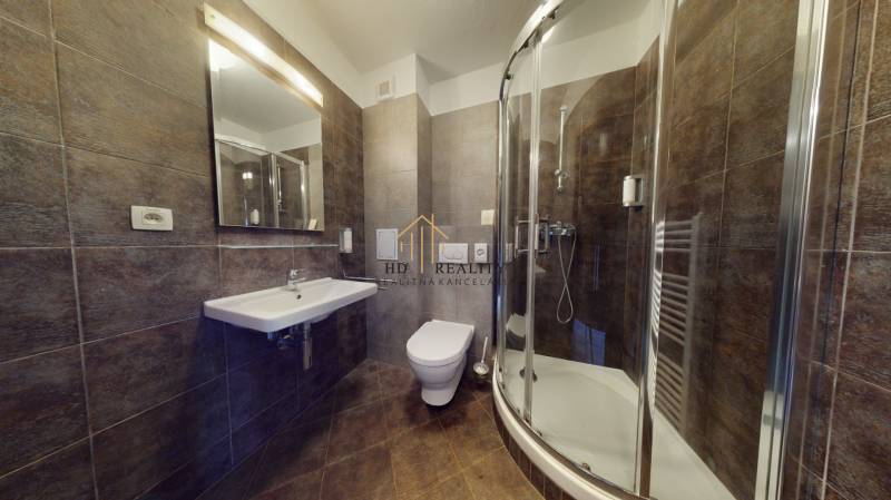 Badezimmer mit dunklen Fliesen, Duschkabine und Toilette in einer Zweizimmerwohnung.
