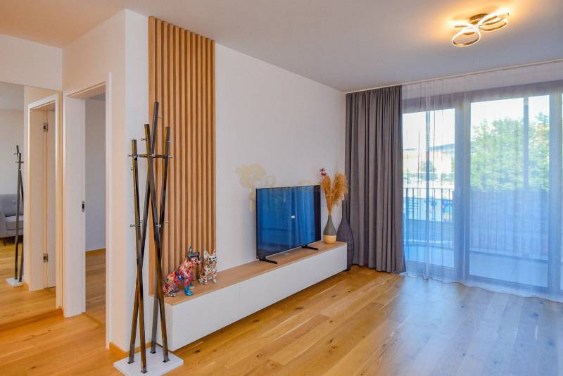 Wohnzimmer in einer 3-Zimmer-Wohnung mit TV, verglastem Balkon und Holzboden.