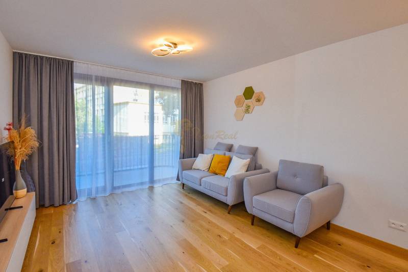 Wohnzimmer mit Holzboden, grauen Möbeln und großem Fenster in einer 3-Zimmer-Wohnung.
