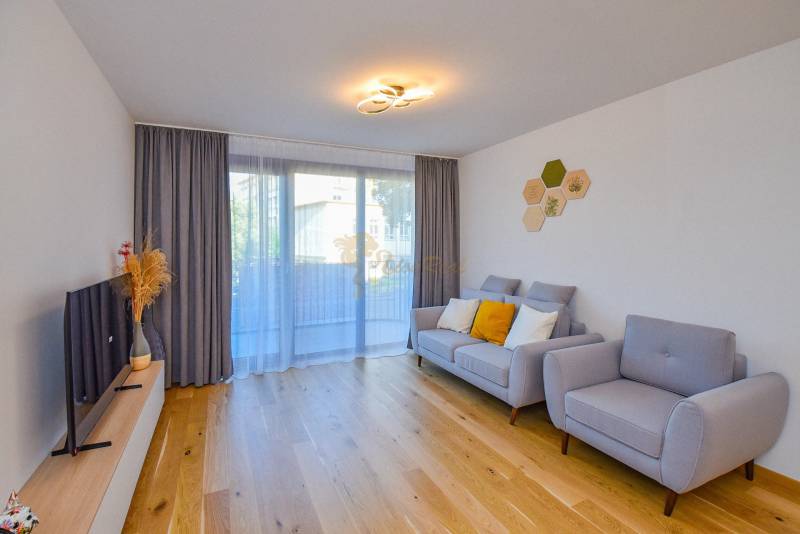 Wohnzimmer mit bequemer Couch, Holzboden und Fernseher in einer 3-Zimmer-Wohnung.