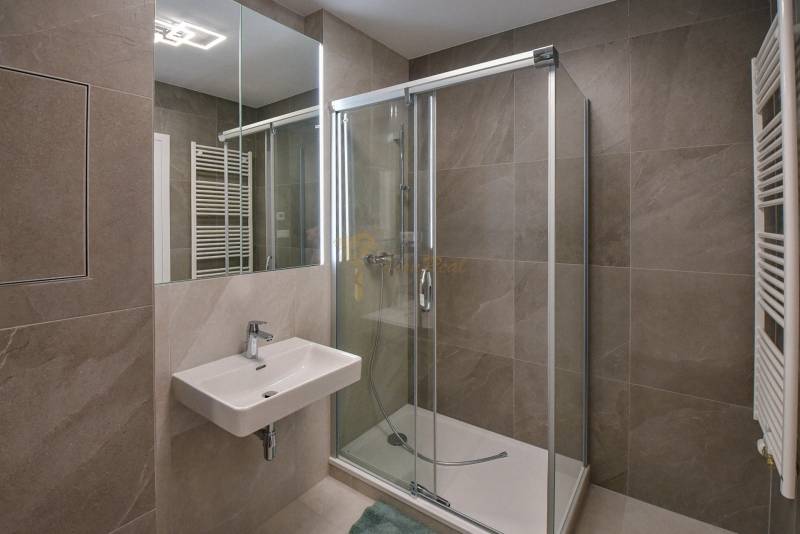 Badezimmer in einer 3-Zimmer-Wohnung mit Waschbecken, Duschkabine und Spiegel mit Fliesen.