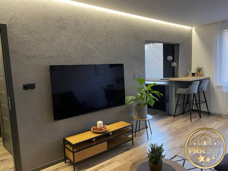 Wohnzimmer in einer 3-Zimmer-Wohnung mit modernem Fernseher, Pflanzen und einer Bar mit hohen Stühlen.