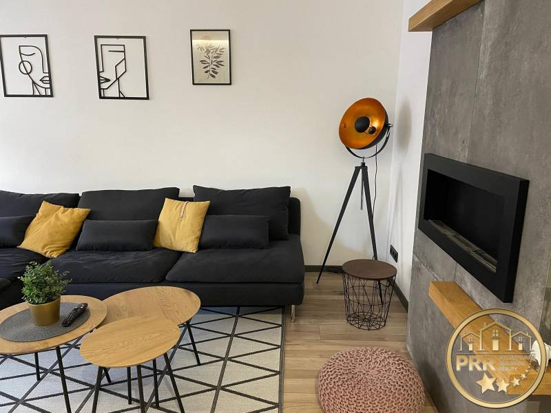 Wohnzimmer in einer 3-Zimmer-Wohnung mit schwarzem Sofa und dekorativer Beleuchtung.