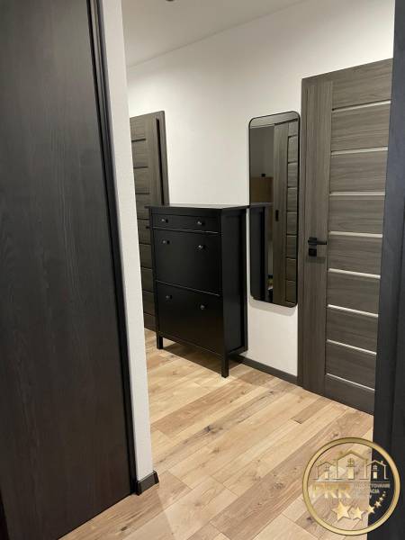Der Flur einer 3-Zimmer-Wohnung mit Holzboden, schwarzer Kommode und Spiegel.