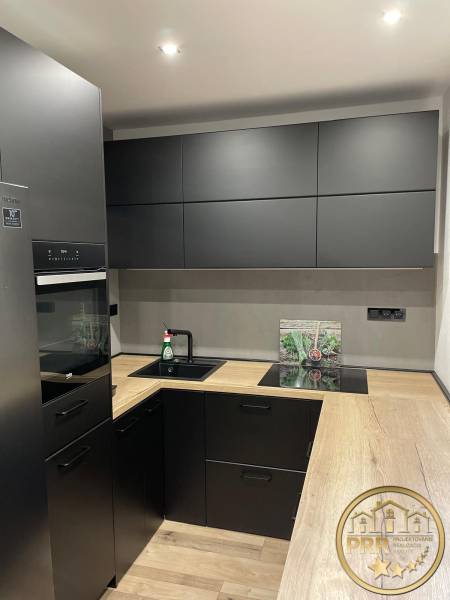 Küche in einer 3-Zimmer-Wohnung mit schwarzen Schränken und einer Holzarbeitsplatte.