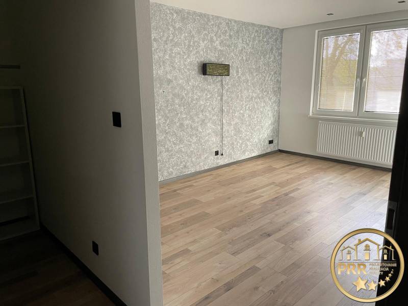 Ein leerer Raum in einer 3-Zimmer-Wohnung mit Holzboden und einer strukturierten Wand.