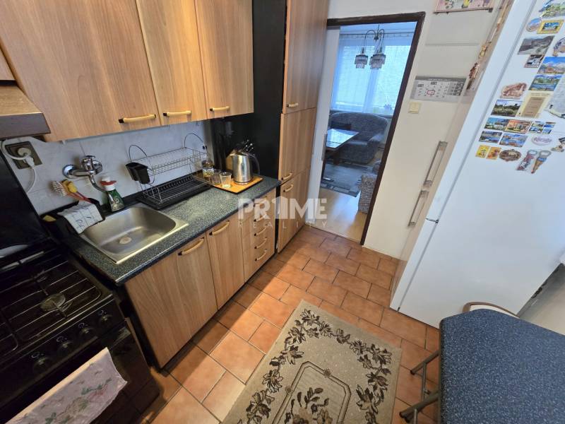 Küche in einer 3-Zimmer-Wohnung mit Holzschränken und Geräten, Raum verbunden mit dem Wohnzimmer.