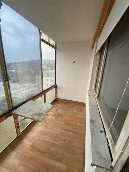 Ein verglaster Balkon einer 3-Zimmer-Wohnung mit Holzboden und Blick auf die Dächer der Gebäude.