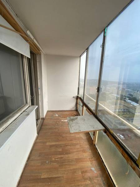 Veranda mit Glasfenstern und Holzboden in einer 3-Zimmer-Wohnung, mit Blick auf das Äußere.