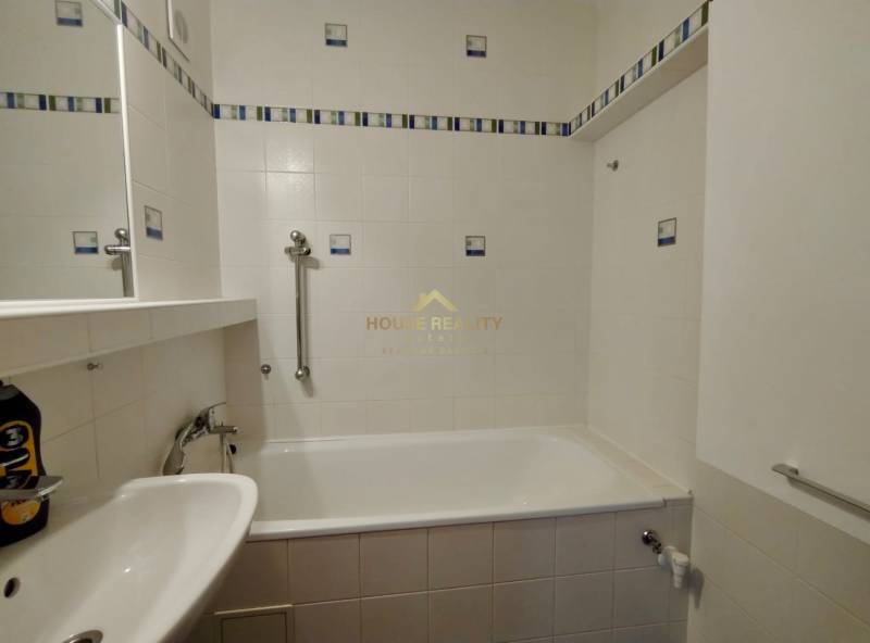 Badezimmer mit Badewanne, weißen Fliesen und Haltegriffen in einer 3-Zimmer-Wohnung.