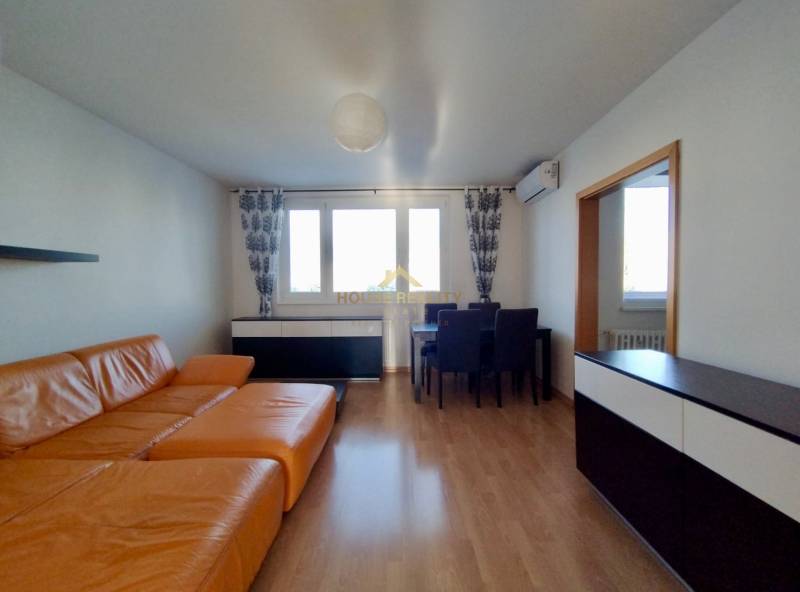 Wohnzimmer in einer 3-Zimmer-Wohnung mit einem orangefarbenen Sofa und einem Boden in Holzoptik.