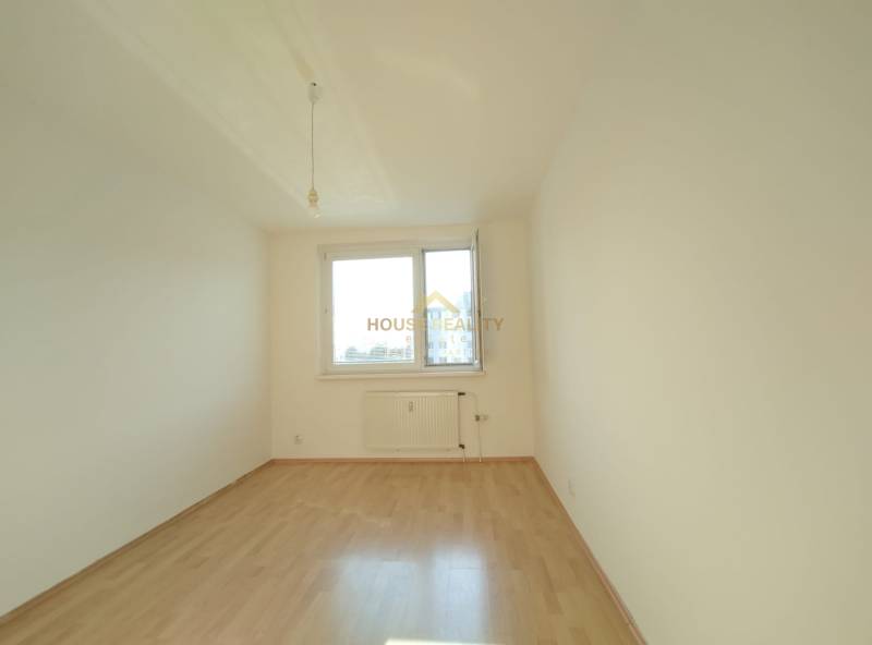 Ein leerer Raum mit einem großen Fenster, weißen Wänden und einem Boden in Holzoptik, 3-Zimmer-Wohnung.