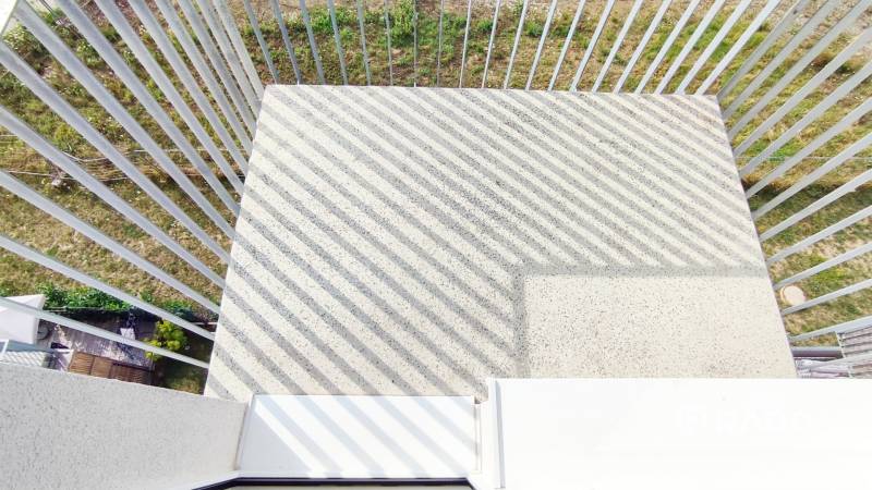 Ein Balkon mit Betonboden und Metallgeländer, der zum Garten ausgerichtet ist.