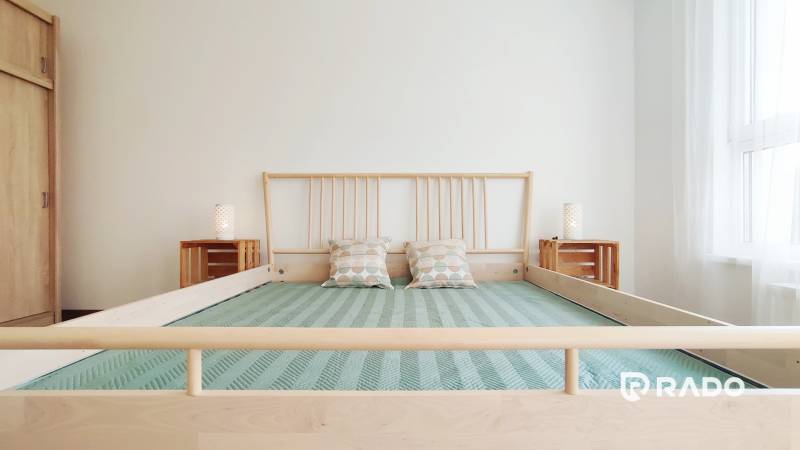 Helles Schlafzimmer mit Holzbett und Kissen in einer Zweizimmerwohnung.