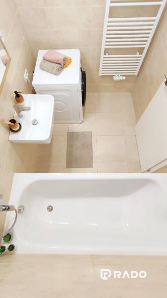 Badezimmer mit Badewanne, Waschbecken, Waschmaschine und Handtuchheizkörper in einer 2-Zimmer-Wohnung.