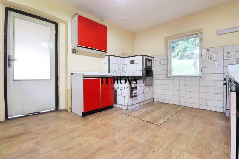 Die Küche eines Einfamilienhauses mit Holzboden, roten Schränken und einem Kachelherd.